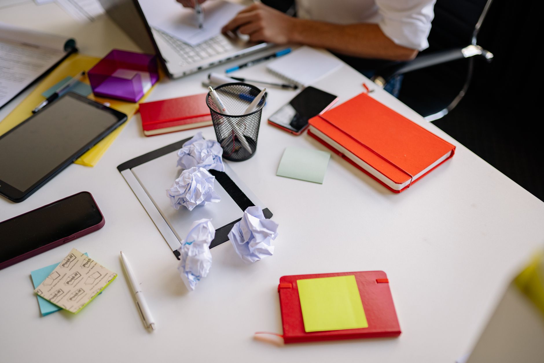 A desk covered in notes, pens and crumpled paper
