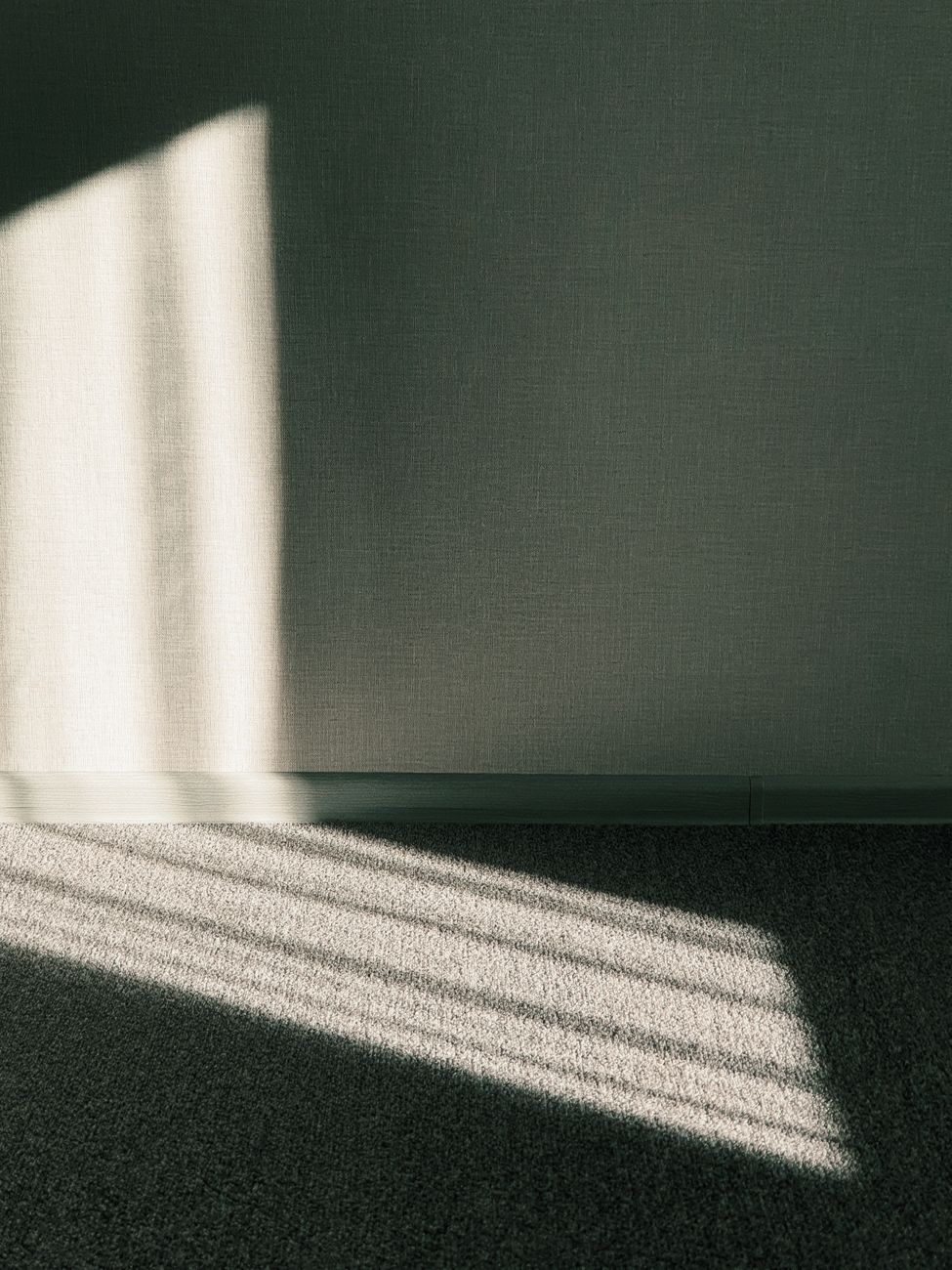 Light from a blind falling across a dark green wall