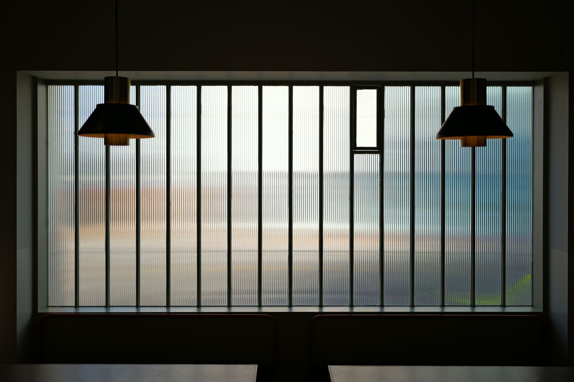 Two pendant lamps in front of a ribbed glass window