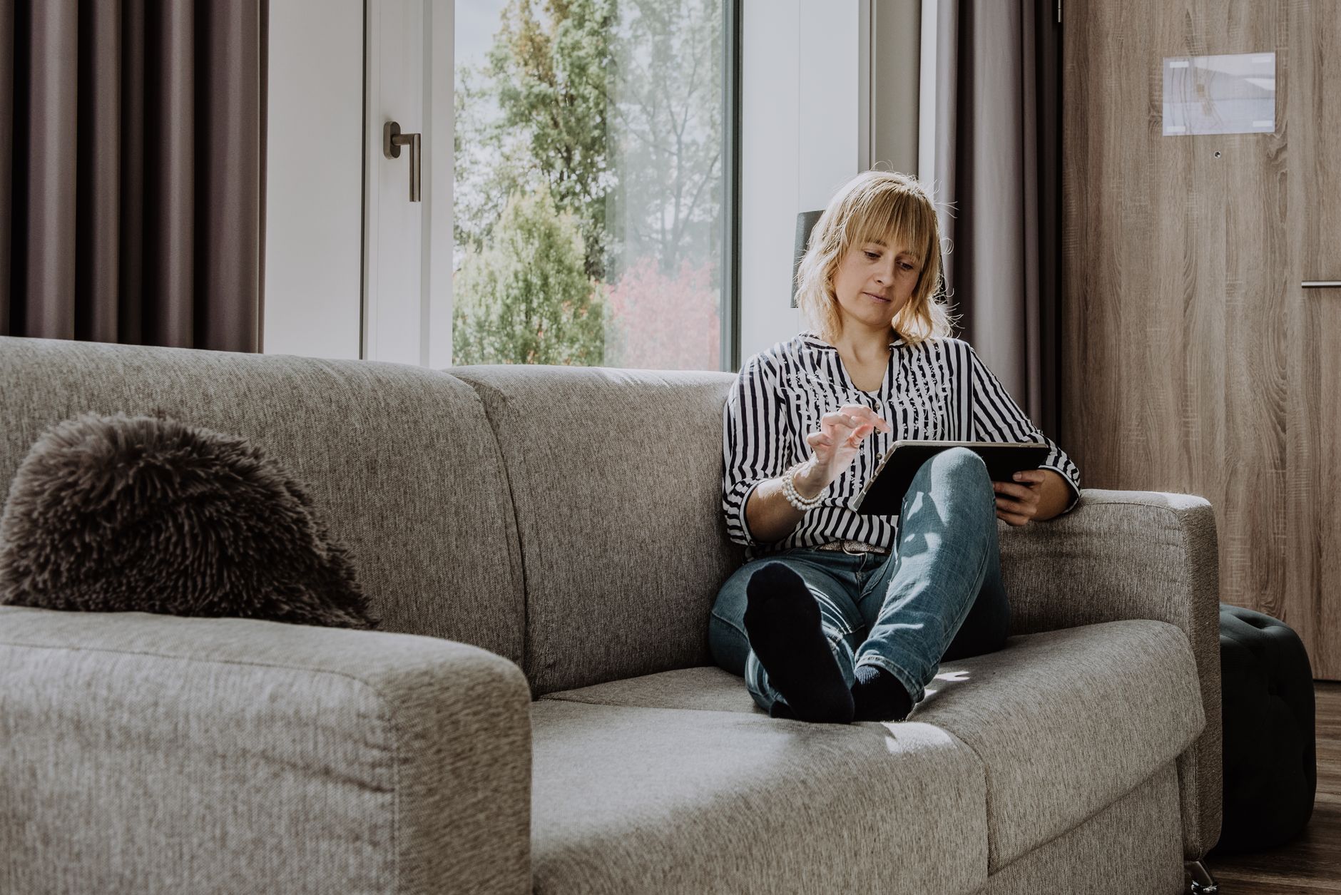 Woman reading floor maps on a tablet on a grey sofa