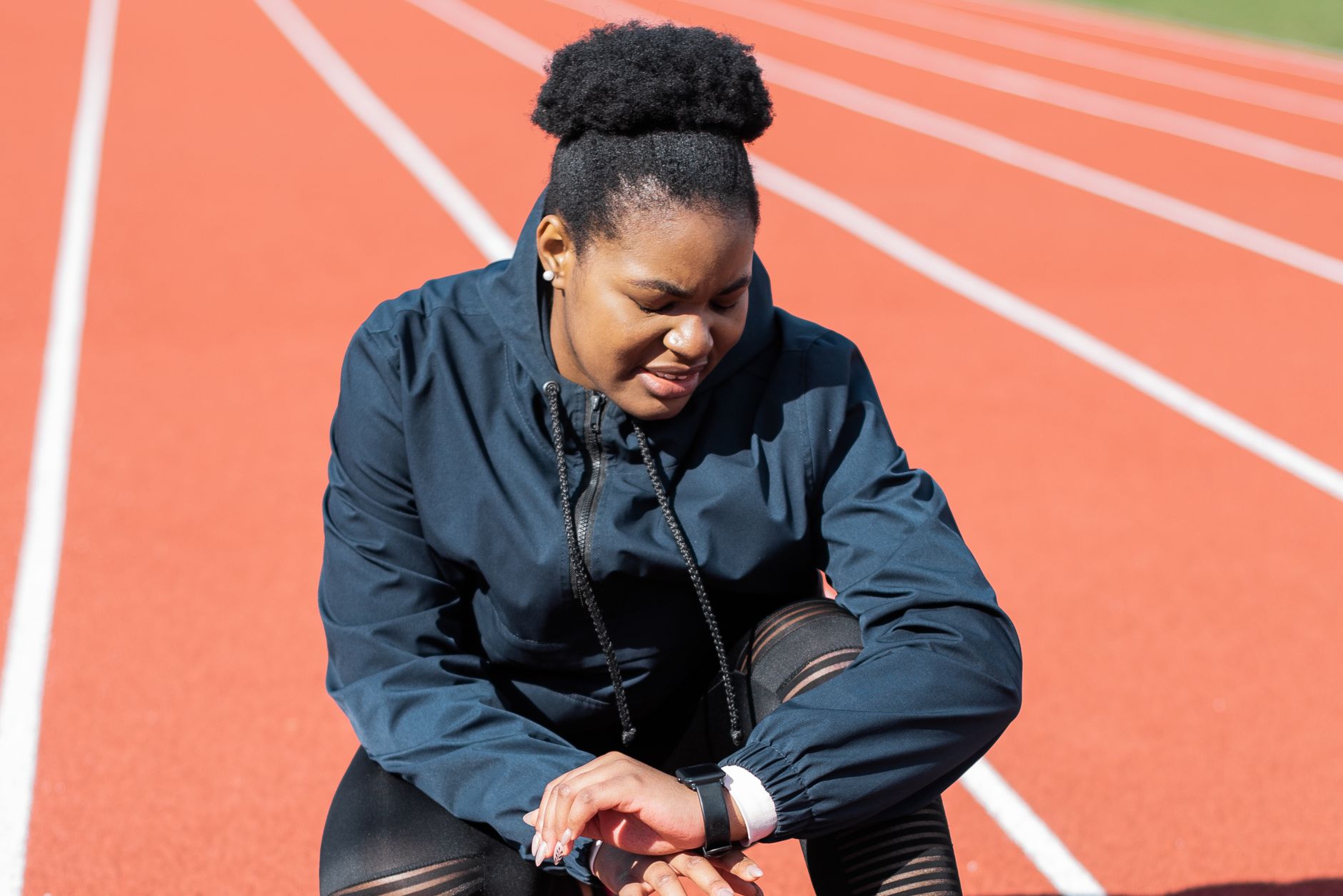 Runner crouching on a red track, checking her watch