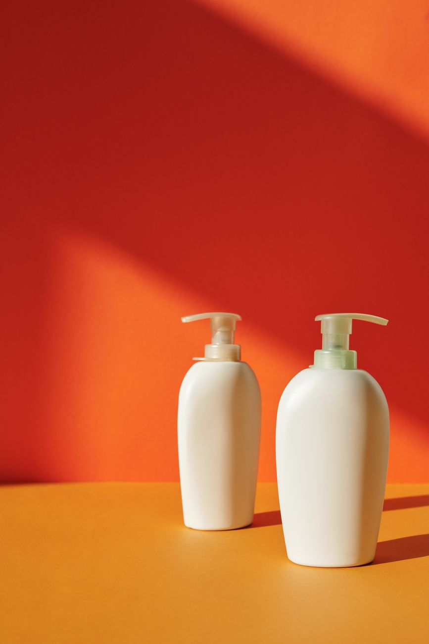 Two white pump bottles on a red and orange ground